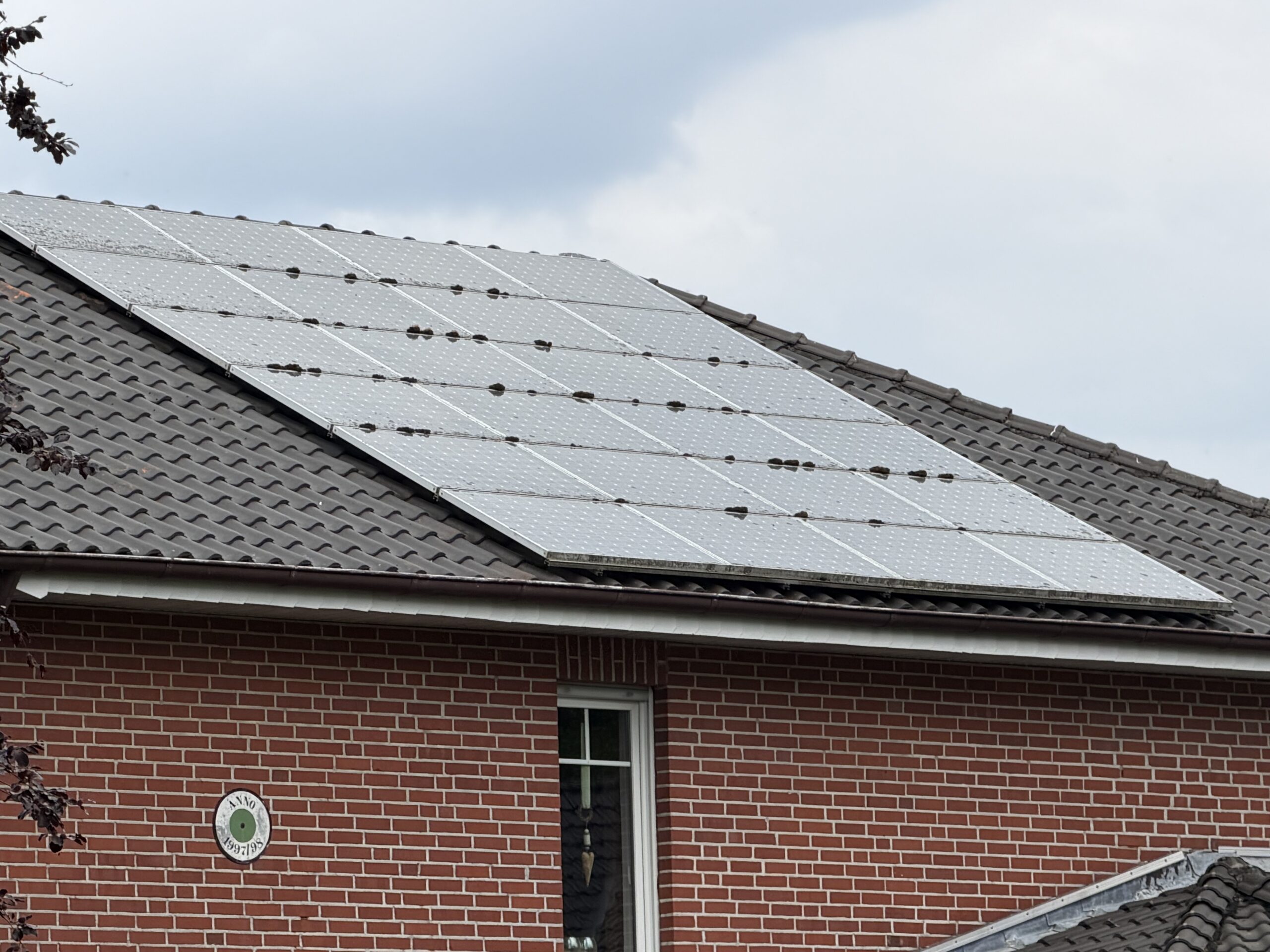 Wohndach mit Sonnenkollektoren, die über der Außenseite eines Backsteinhauses in einem Vorort installiert sind.